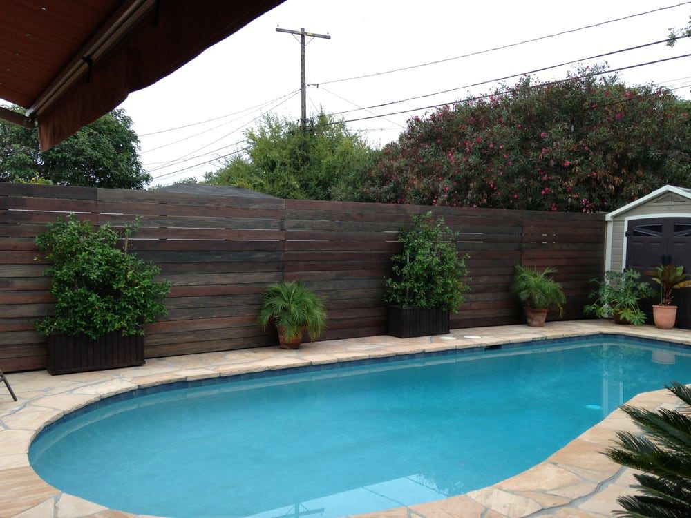 Modern wood horizontal fence with greenery by a pool, meeting Kentucky pool fence regulations and swimming pool barrier standards.