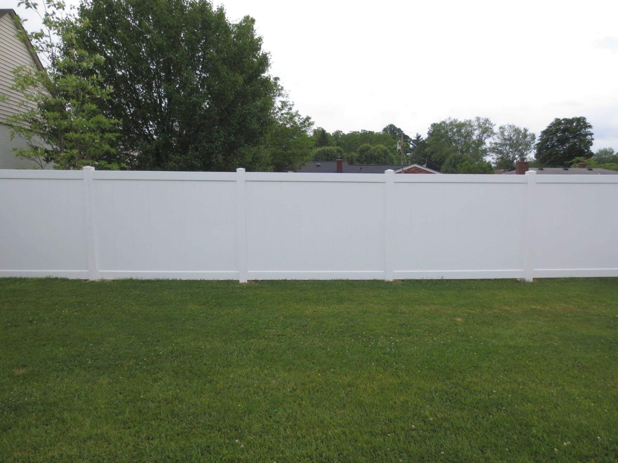 White vinyl privacy fence enclosing a flat backyard lawn