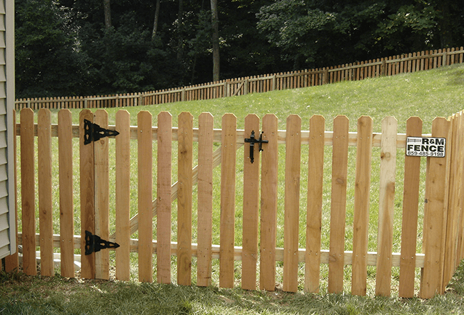 Wooden picket fence gate with black hardware on grassy yard