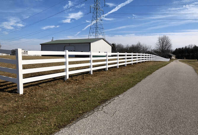 White vinyl farm fence along rural property with barn and gravel drive