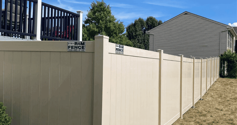 Tan vinyl privacy fence installed on a sloped residential yard