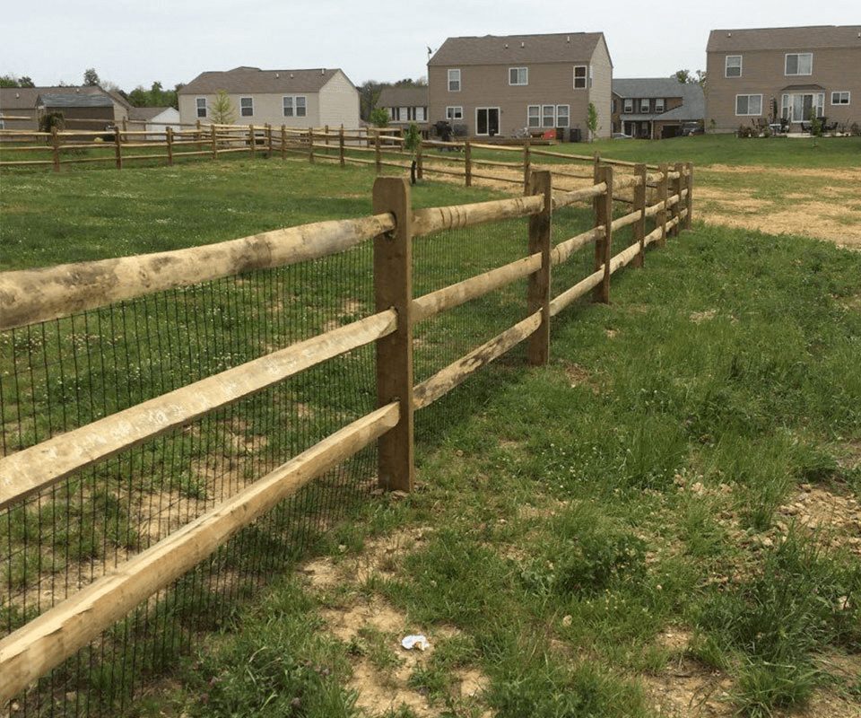 Split rail fence with attached wire mesh defining backyard space in a neighborhood setting