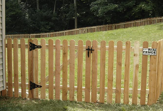 Wooden picket fence gate with black hardware on grassy yard