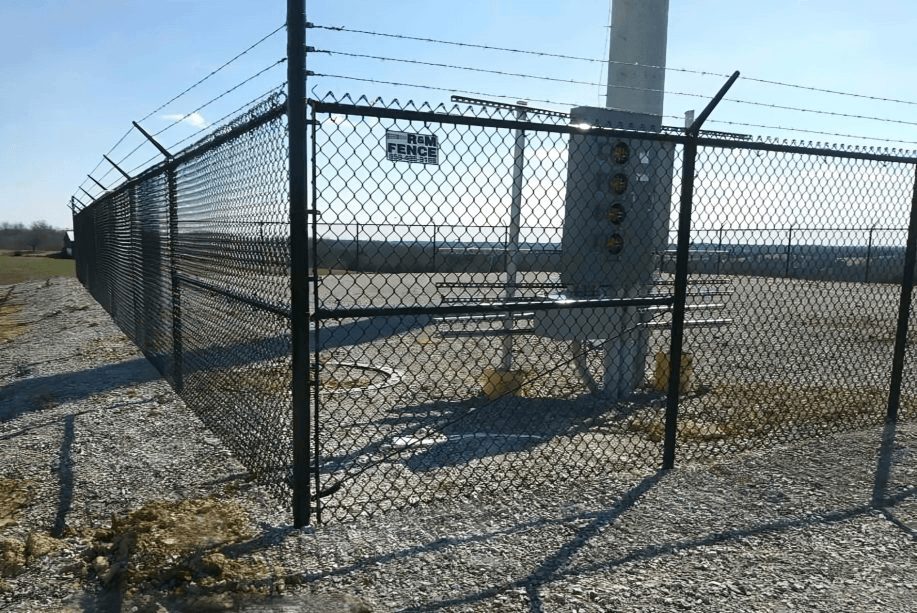 Black chain link security fence enclosing utility equipment on gravel lot
